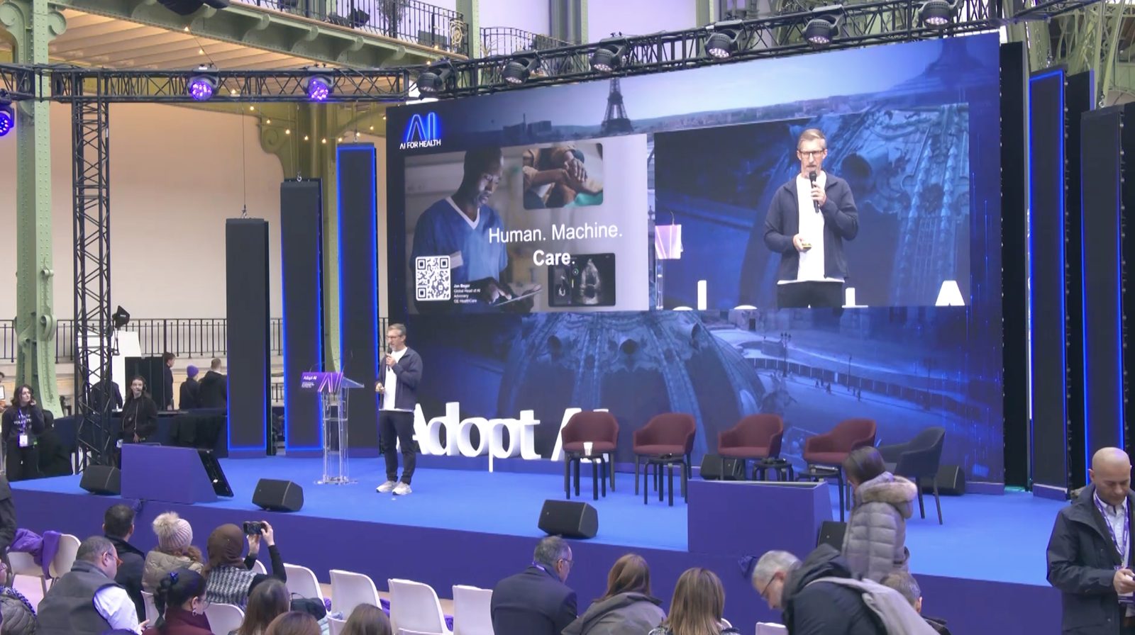 Jan Beger keynoting at Adopt AI, Grand Palais, beside a Human. Machine. Care. screen